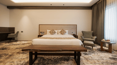 A guest room featuring a king-sized bed, a wooden bench, and a work desk area with an armchair at Ananta Express, Katra.