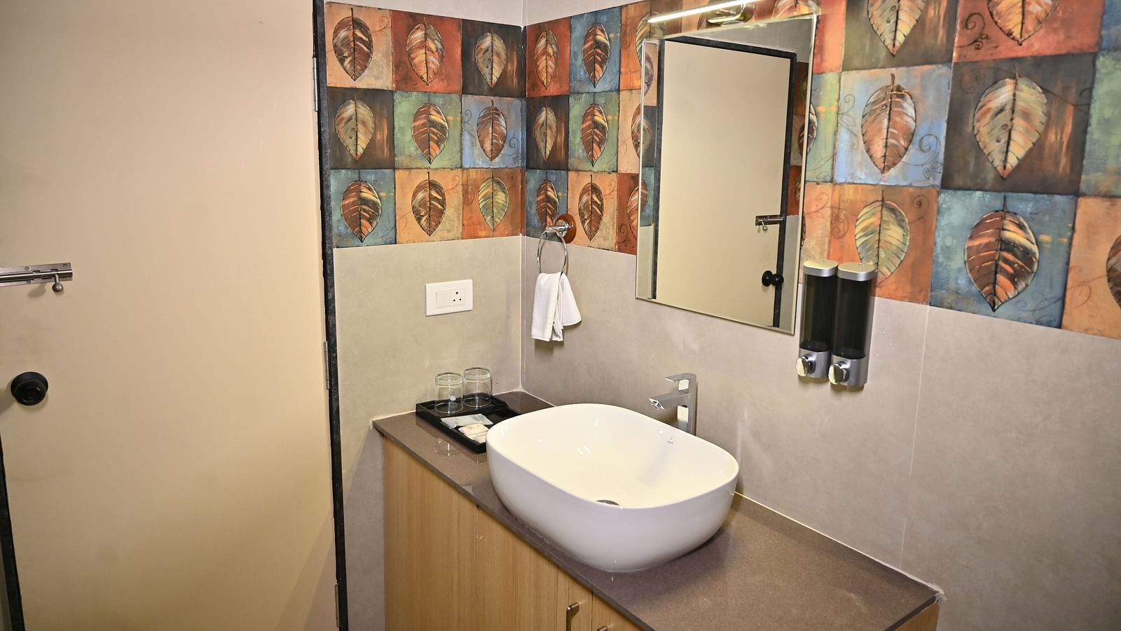 Bathroom with a colourful leaf-patterned tile design, a wash basin, a mirror, and a neatly organised countertop at TGI Livancia Hillside