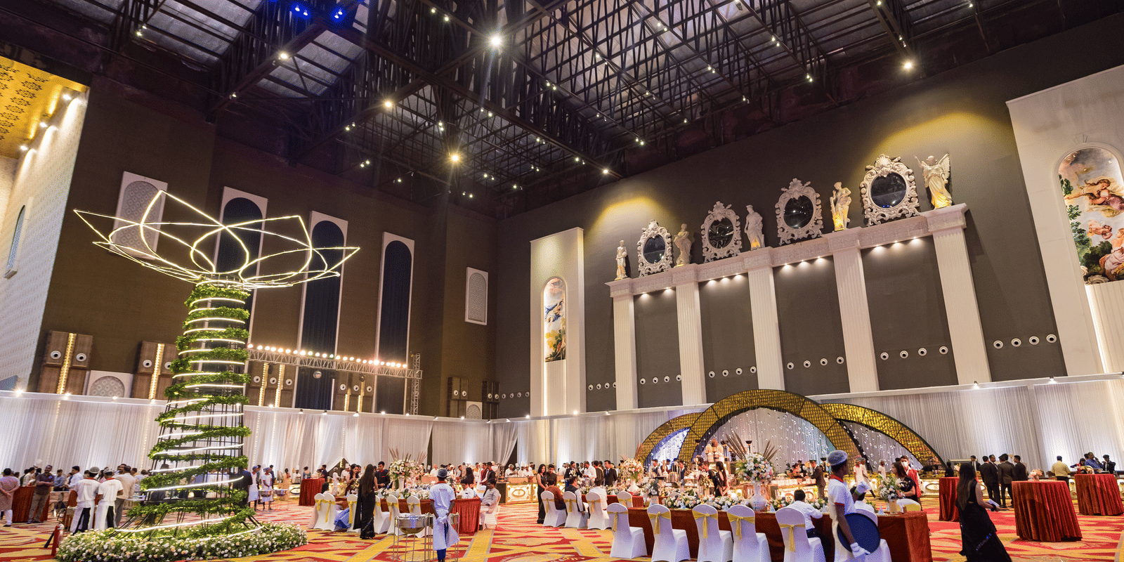 Vast, high-ceilinged convention or banquet hall decorated for an event with a large hanging ornament and a crowd of people at Hotel Hukam's Lalit Mahal.