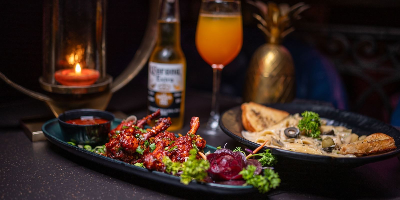 A plate of delicious food accompanied by a beer bottle and a glass of drink, all beautifully arranged with a candle for a cozy atmosphere at hotel moti palace.