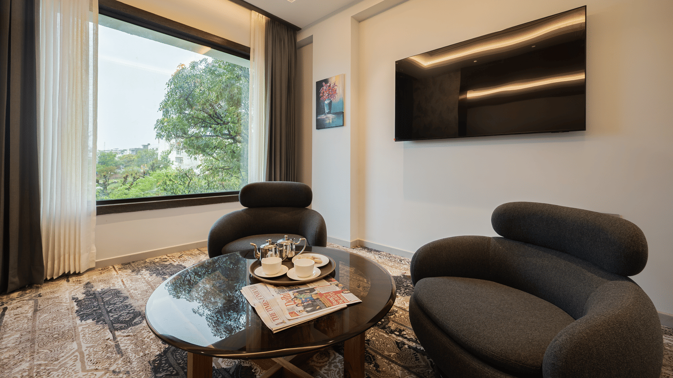 A suite living area featuring a round glass coffee table, a curved sofa, and a wall-mounted television at Ananta Express, Katra.