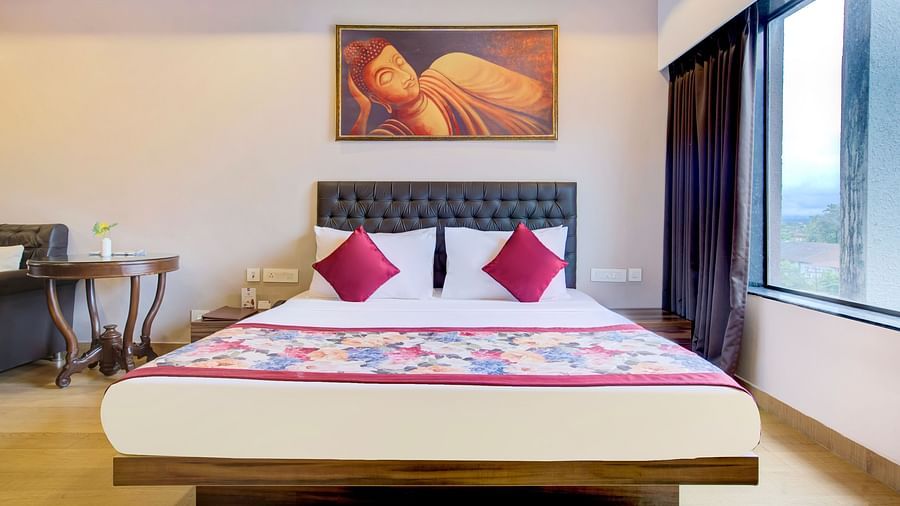 Elegant bedroom featuring a vibrant bedspread, wall art, and a large window with city views at Voyage Milestone Hotel and Banquet Siliguri