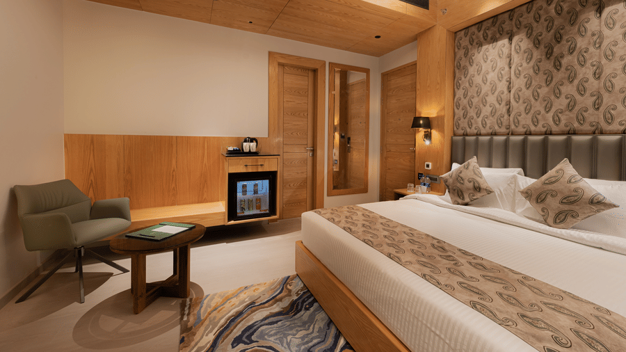 A guest room featuring a king-sized bed, a green armchair, and a wooden cabinet with a minibar at Ananta Express, Katra.