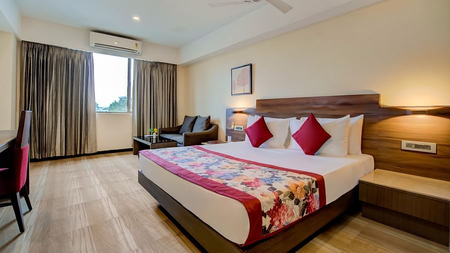 Spacious room with a double bed, lounge chairs, and natural light from large windows at Voyage Milestone Hotel and Banquet Siliguri