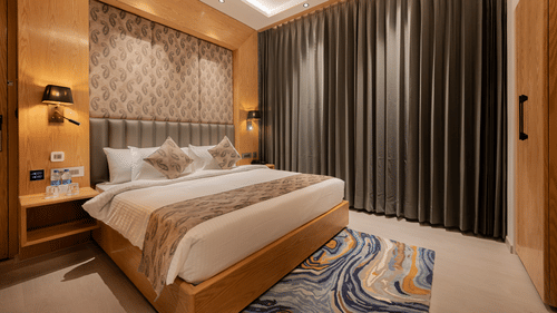 A bright guest room featuring a king-sized bed with a patterned headboard and floor-to-ceiling grey curtains at Ananta Express, Katra.