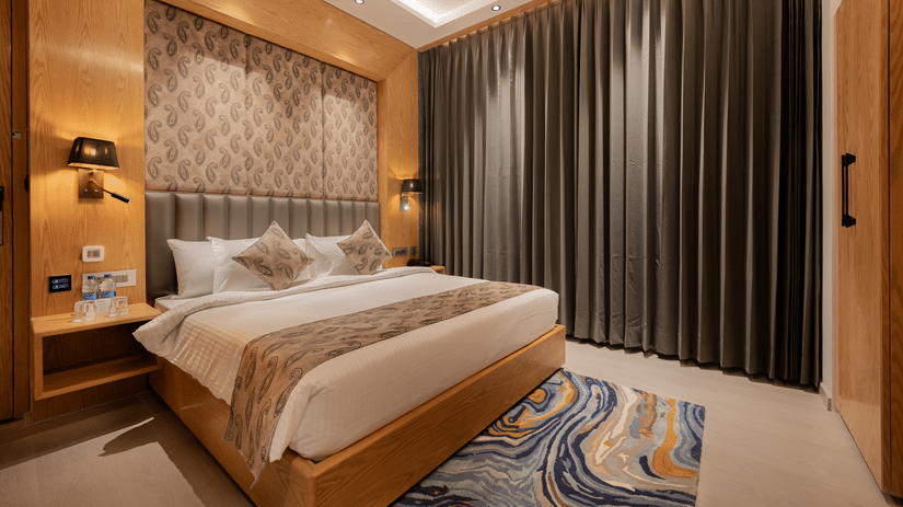 A bright guest room featuring a king-sized bed with a patterned headboard and floor-to-ceiling grey curtains at Ananta Express, Katra.