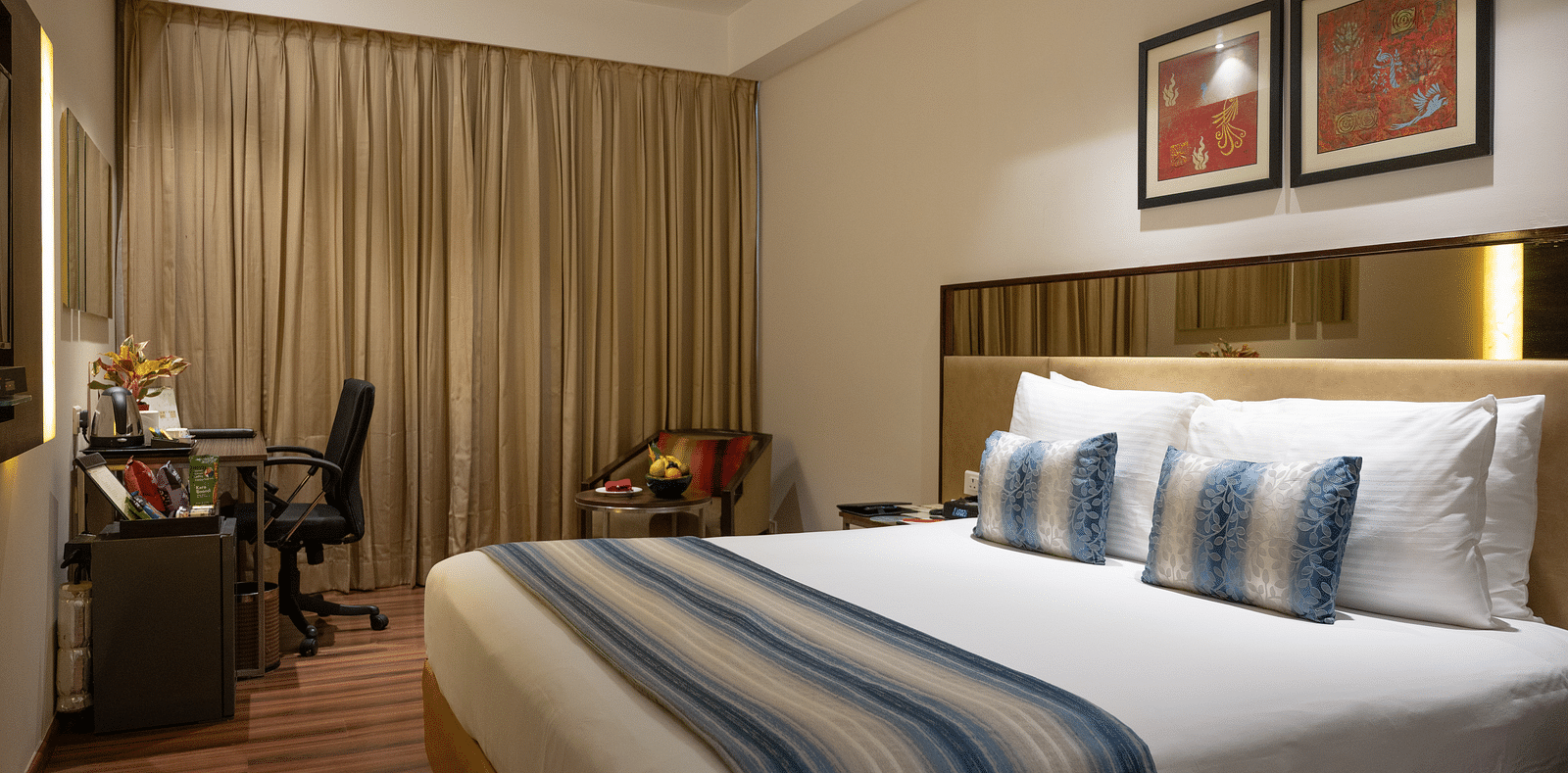 An image of a bedroom with working table and a chair at long shot view of the hotel corridors at Grand Kakinada by GRT Hotels