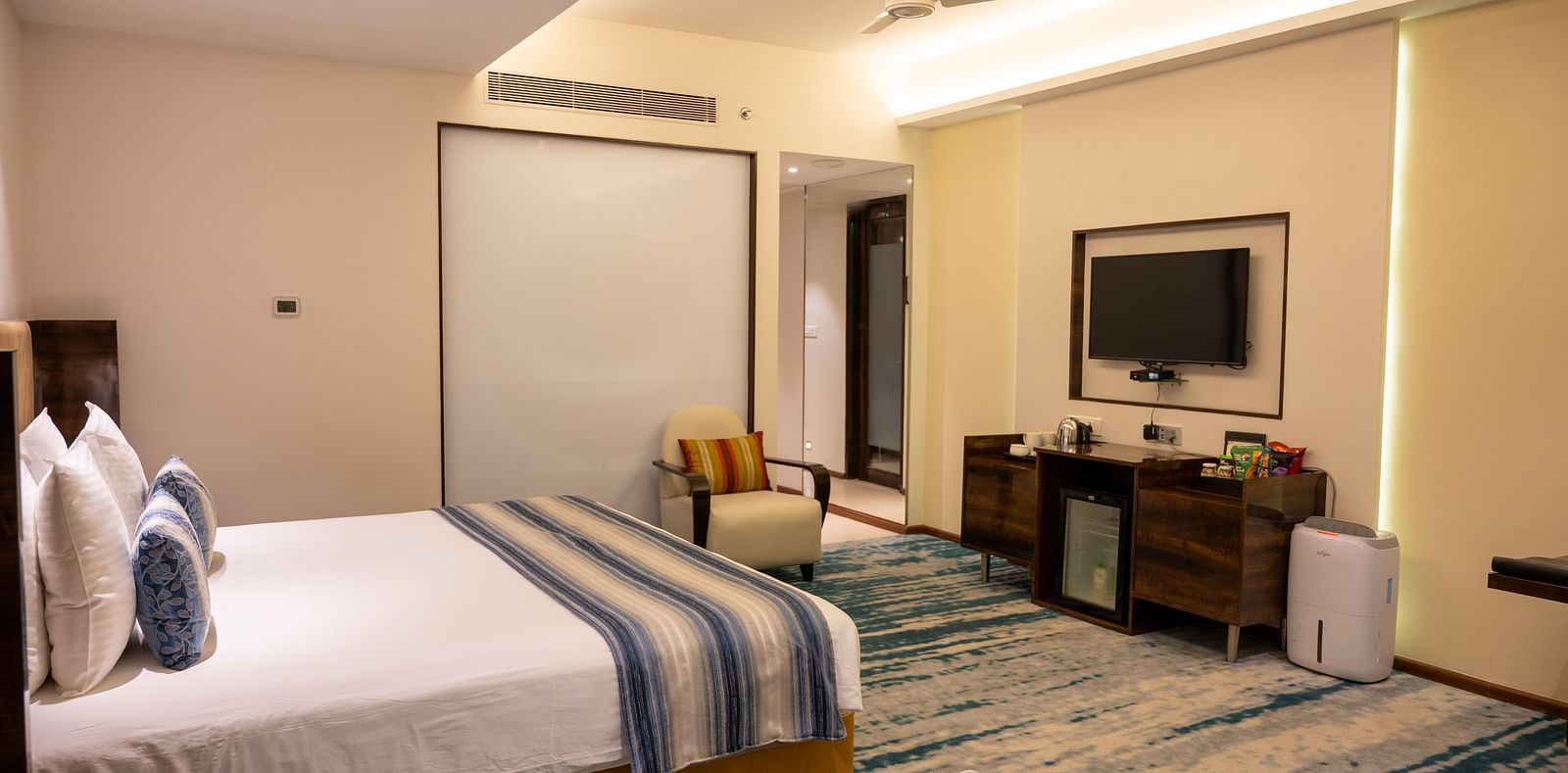 An image of a bedroom with a fan and a wall mounted television at Grand Kakinada by GRT Hotels