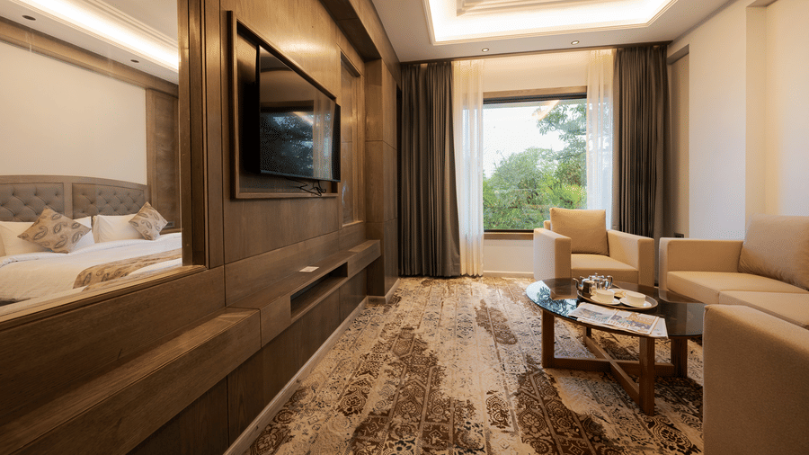 A modern guest suite featuring a king-sized bed, a wall-mounted television, and a window with a green landscape view at Ananta Express, Katra.
