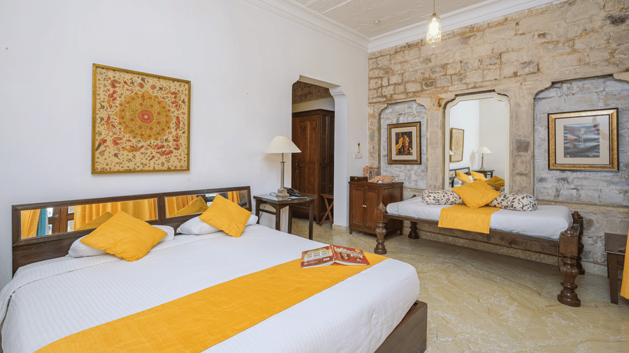 A spacious bed with yellow runner and daybed against a stone wall in Aruna Vilas at Deo Bagh - 17th Century, Gwalior.