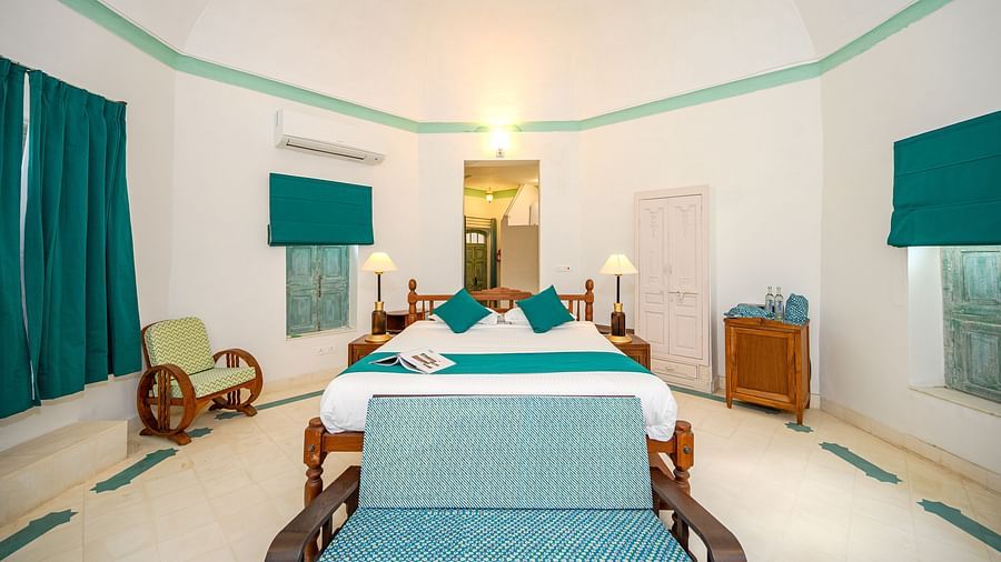A long shot of a room with white walls and a table with a runner, chair in the centre and window on the left side with a blind on - Tijara Fort-Palace - 19th Century, Alwar