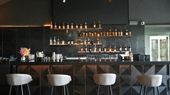 Modern bar at Hotel Daspalla, Hyderabad with black marble backdrop, premium spirit display on lit shelves, white bar stools, and curved wooden ceiling beams with warm lighting.
