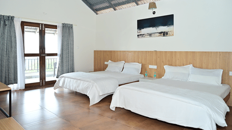 2 king size beds with white bedding, side by side in a room with a wall-mounted painting and glass doors at Aarika Resort & Hotels.