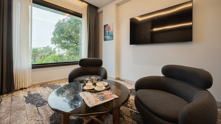 A suite living area featuring a round glass coffee table, a curved sofa, and a wall-mounted television at Ananta Express, Katra.