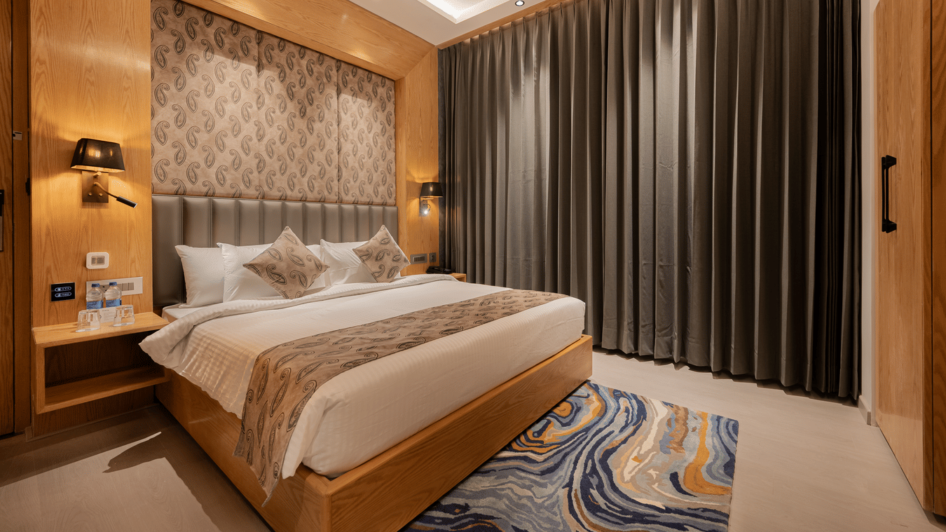 A bright guest room featuring a king-sized bed with a patterned headboard and floor-to-ceiling grey curtains at Ananta Express, Katra.