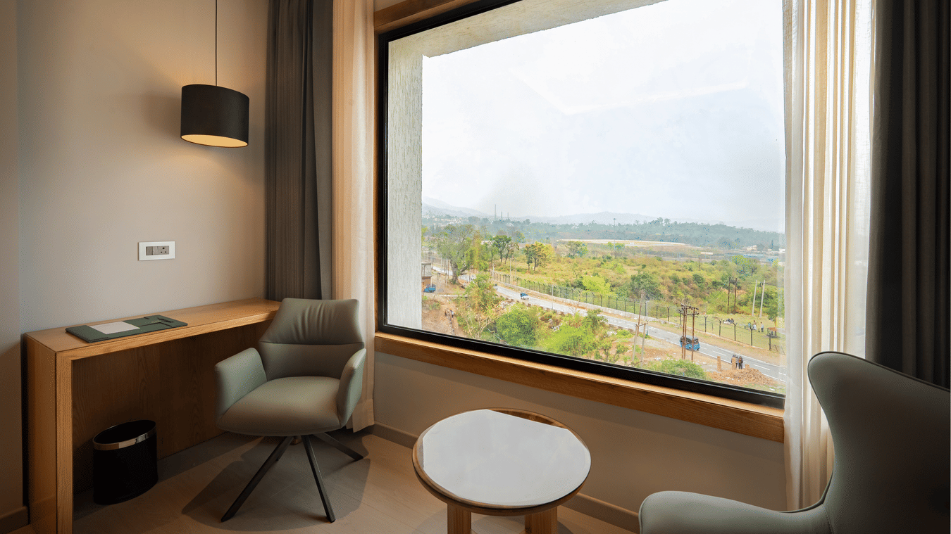 A modern bedroom corner featuring a green armchair and a large window overlooking a lush landscape at Ananta Express, Katra.