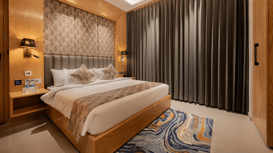 A bright guest room featuring a king-sized bed with a patterned headboard and floor-to-ceiling grey curtains at Ananta Express, Katra.