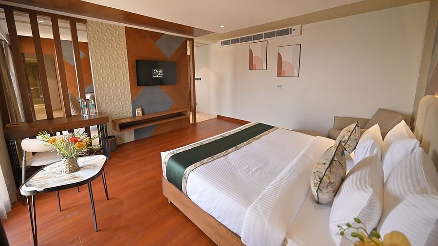 A bedroom with a bed facing a wall-mounted television and a table with a flower vase placed beside the bed at  Clarks Collection Grand Sapphire, Ajmer