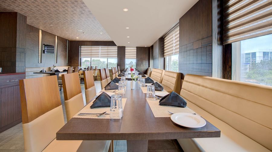 Well-arranged dining tables in a contemporary setting with large windows at Voyage Milestone Hotel and Banquet Siliguri