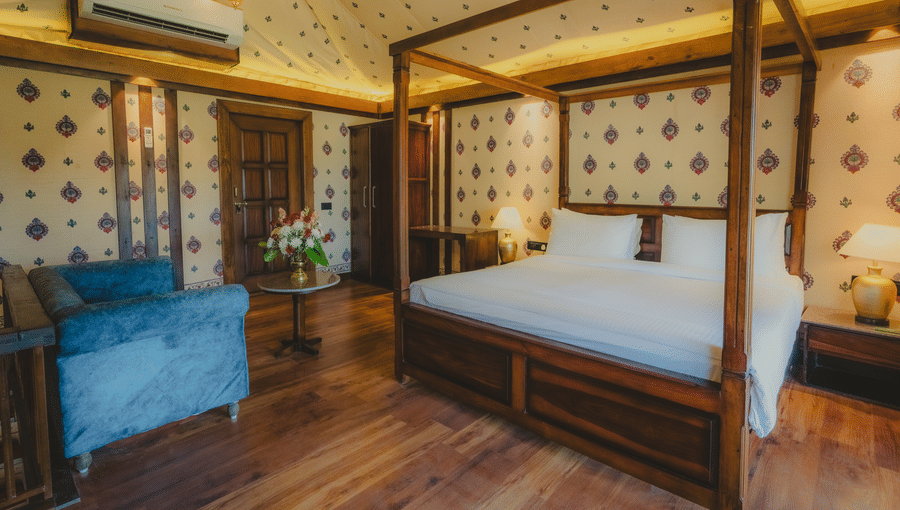 A Premium Duplex Tent bedroom featuring a sofa, a poster bed, bedside table with lamps on either side, cabinet table, a wardrobe, and a centre table with flower vase at The Baagh Ananta Elite, Ranthambore