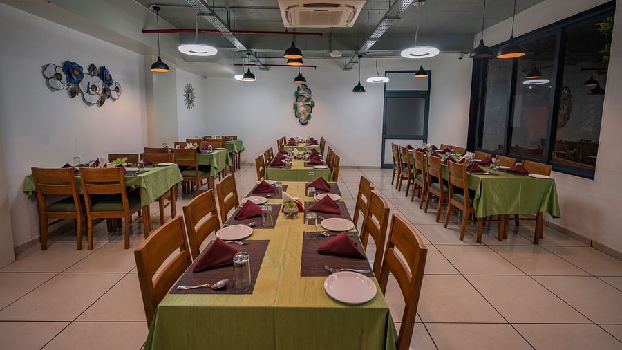 Clarks Safari Kheda's dining area with multiple tables are set with neat coverings and chairs, lights, ac, neatly arranged tissues, plates, spoons, a small money plant on the centre and decorative elements on the walls.
