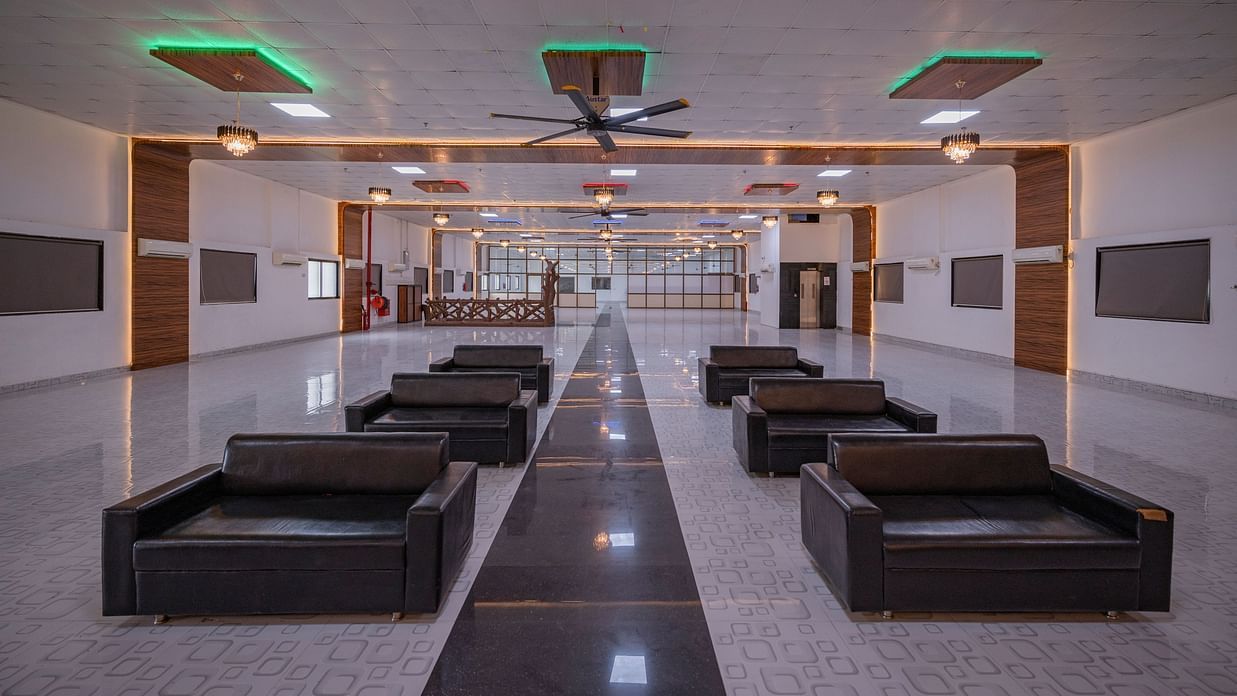 A long, open hall at Clarks Safari Kheda, set up with numerous seating arrangements, leading towards an exit.