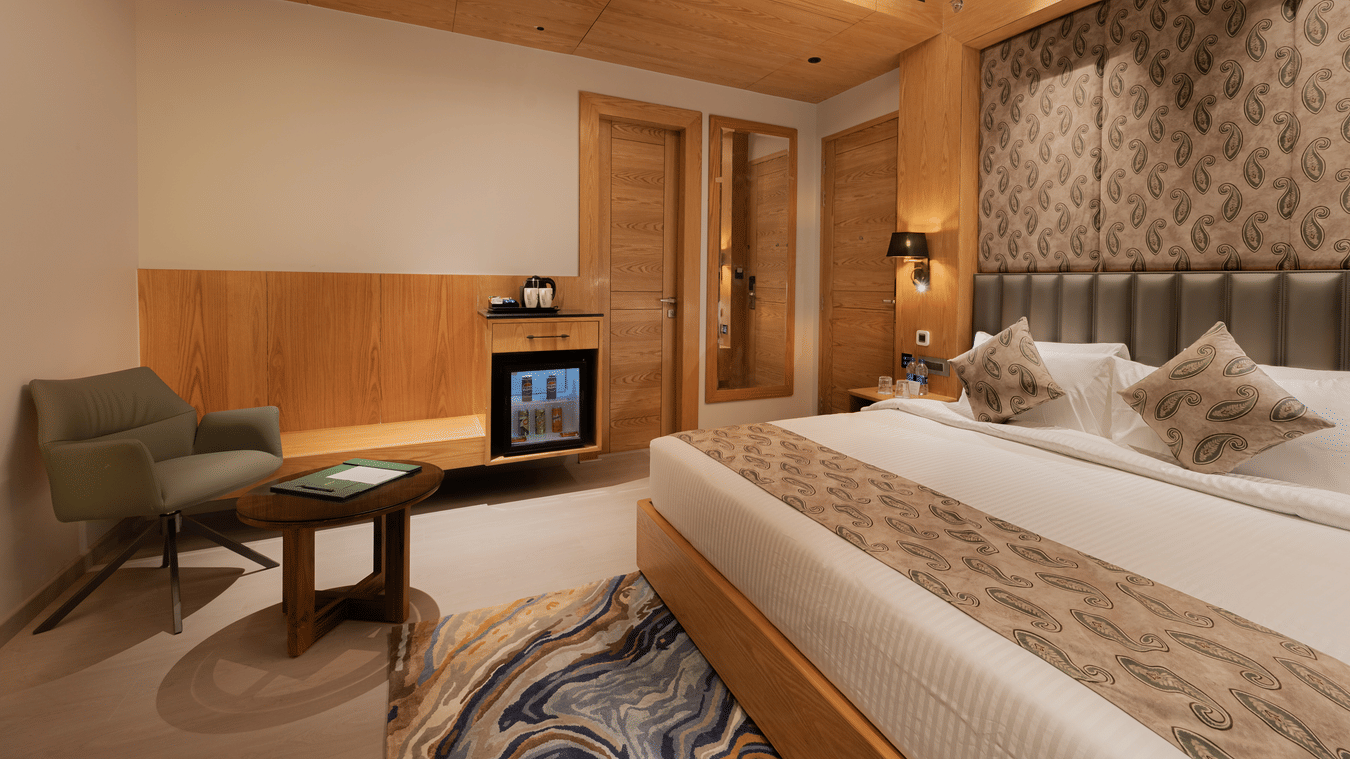 A guest room featuring a king-sized bed, a green armchair, and a wooden cabinet with a minibar at Ananta Express, Katra.