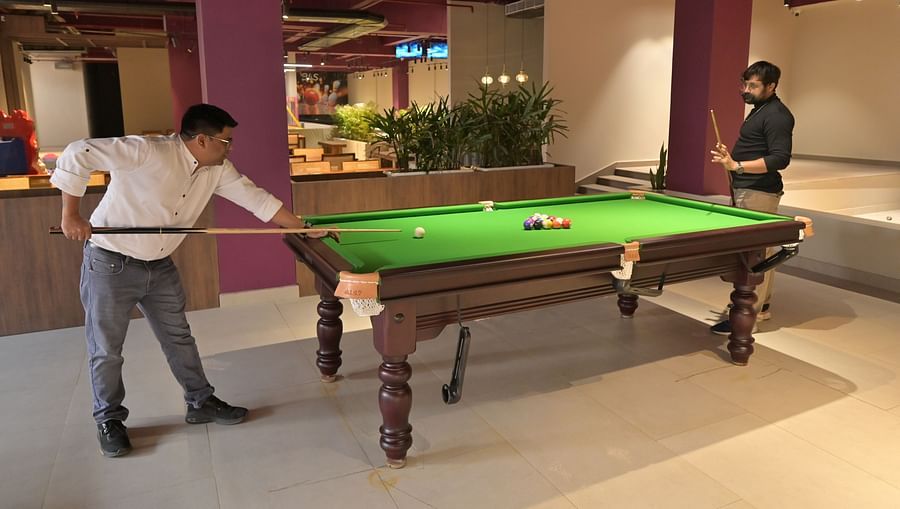 Two men playing snooker around a snooker table, the room having indoor plants in small bushes here and there - Clarks Safari, Haridwar