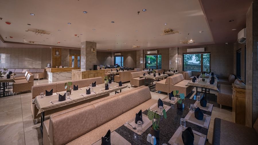 The lounge-style seating area with cushioned arm sofas, tables wit neatly arranged plates, spoon, glass and elegant lighting at Clarks Collection Somnath.