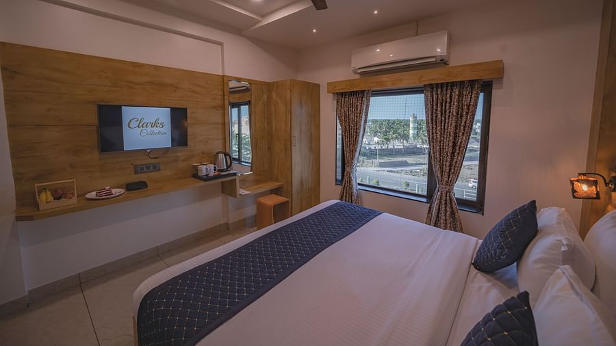 The view of a modern bedroom with ambient lighting, double bed, ac, fan, and a tv unit at Clarks Collection, Somnath.