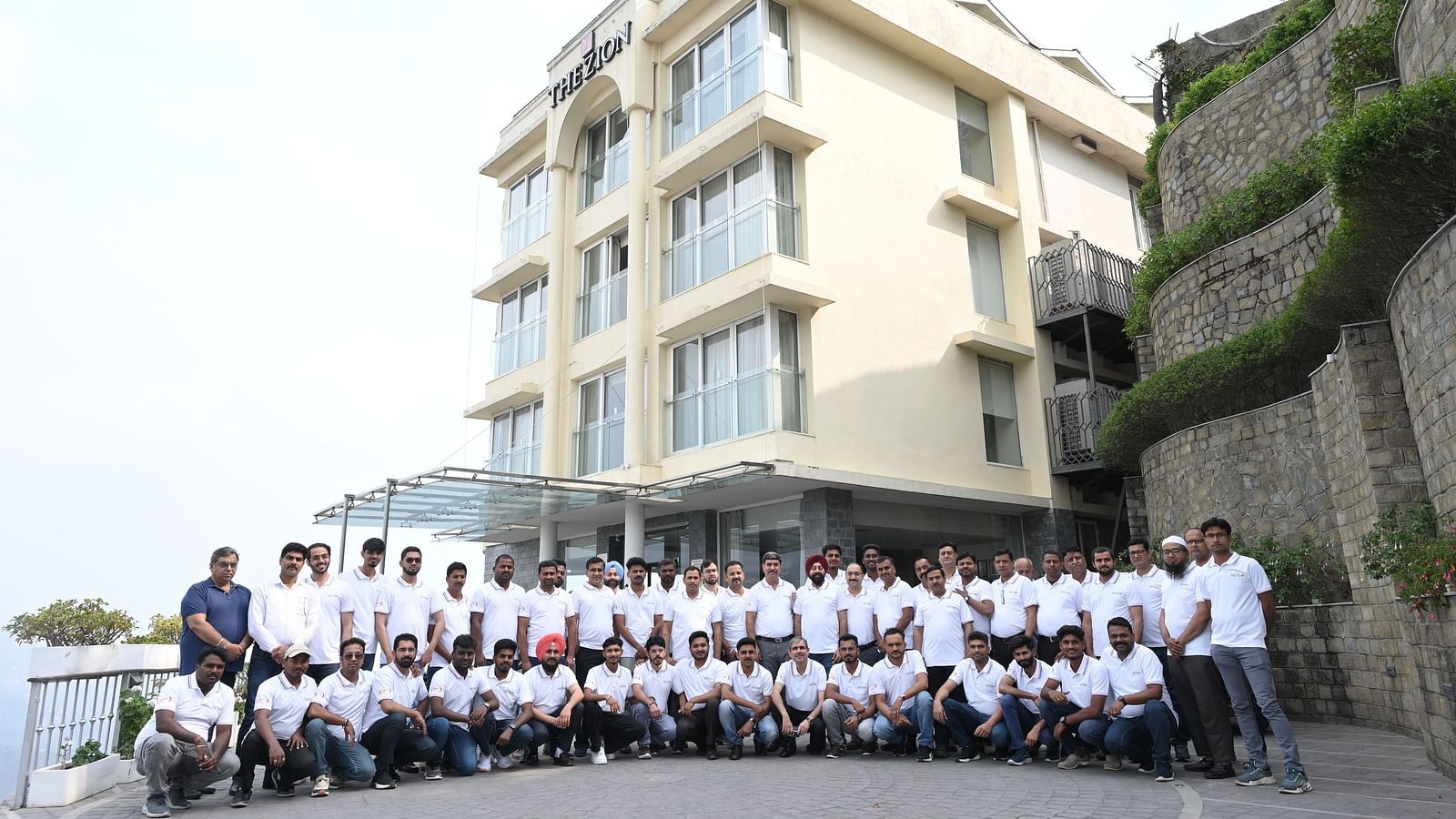 A large group in matching 'Refex' shirts poses for a photo outside The Zion hotel.