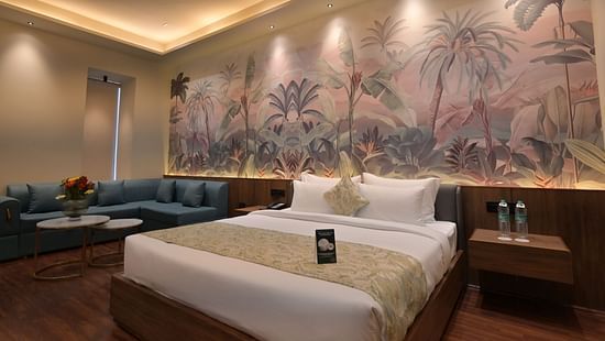 Premium Room featuring  a king size bed with white linens and a patterned throw, a blue corner sofa, and a large mural of a jungle scene on the wall behind the bed. - Clarks Safari Haridwar