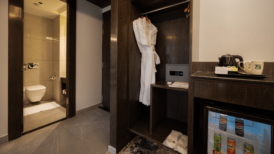 A wooden wardrobe area in a guest room featuring white bathrobes, a digital safe, and a minibar at Ananta Express, Katra.