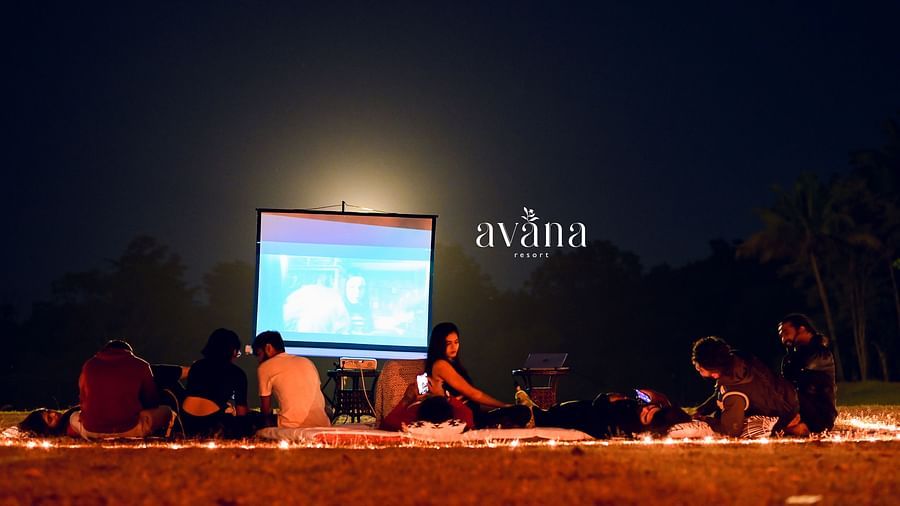 A group of people gathered outdoors at night, possibly watching a movie or performance on a screen.