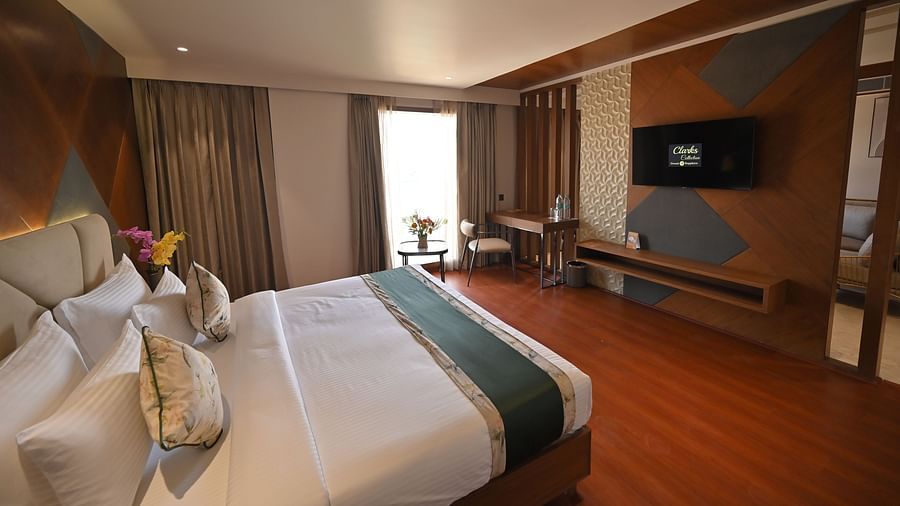 Side view of the bedroom featuring a wall-mounted television and a window with partially drawn curtains at Clarks Collection Grand Sapphire, Ajmer.