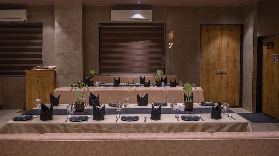 Rectangular table set with tissue, surrounded by cushioned beige seating and brown wall panels at Clarks Collection Somnath.