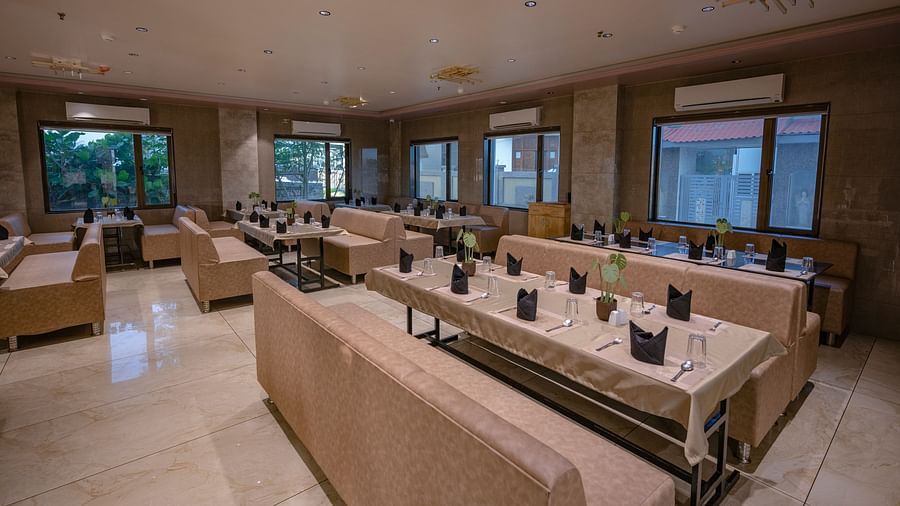 The lounge-style seating area with cushioned arm sofas, tables wit neatly arranged plates, spoon, glass and elegant lighting at Clarks Collection Somnath.