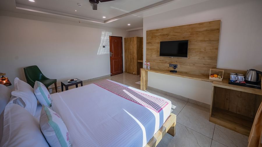 A bedroom with ceiling fan, double bed, chair, table, desk, kettle and mounted TV facing the bed at Clarks Collection, Somnath.