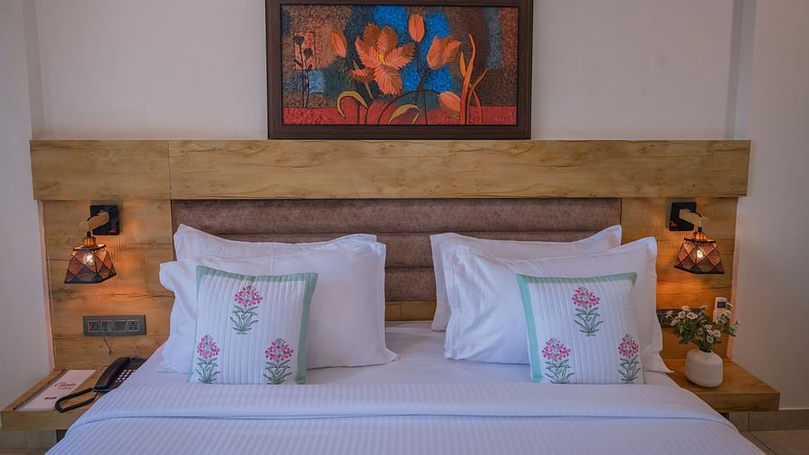 The front view of a double bed with floral pillows, lamps, and wall art above at Clarks Collection, Somnath.