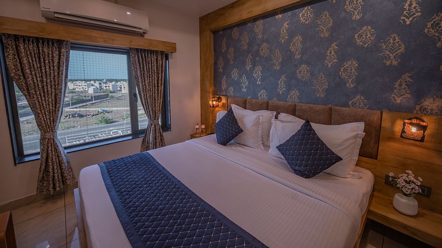 Spacious room with a double bed, ac, water bottles, bedside table with flower vase on the top and city view window at Clarks Collection, Somnath.
