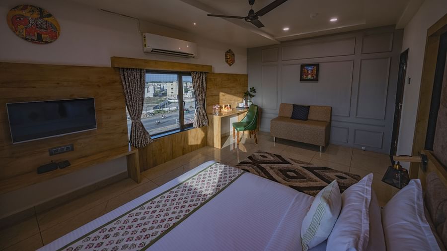 A bedroom at Clarks Collection Somnath with wall-mounted TV, double bed, wooden paneling, rug, chair, and ceiling fan.