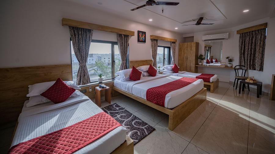 Triple-bed room at Clarks Collection Somnath with large windows, red runners, wooden furniture, fan, curtains, and desk.