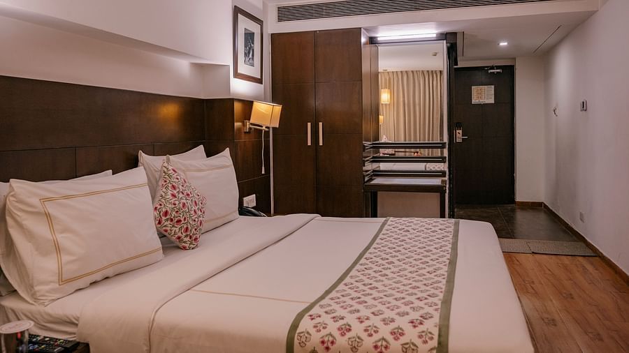 A room with double bed, wooden flooring, lamps, frame, remotes, wardrobe, and mirror at Clarks Collection, Vadodara.