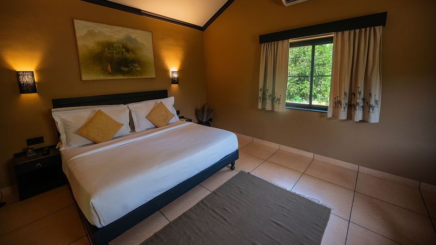 Interior view of a hotel room featuring a double bed with yellow pillows, brown walls, a curtained window, and wall-mounted lights - Clarks Safari, Pushkar