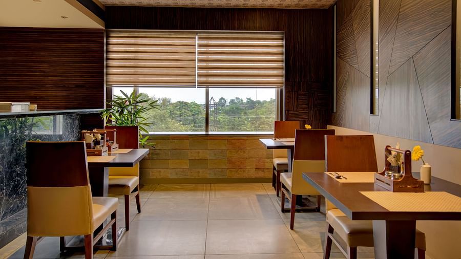 Corner restaurant seating with a view, wooden décor, and a cosy dining atmosphere at Voyage Milestone Hotel and Banquet Siliguri