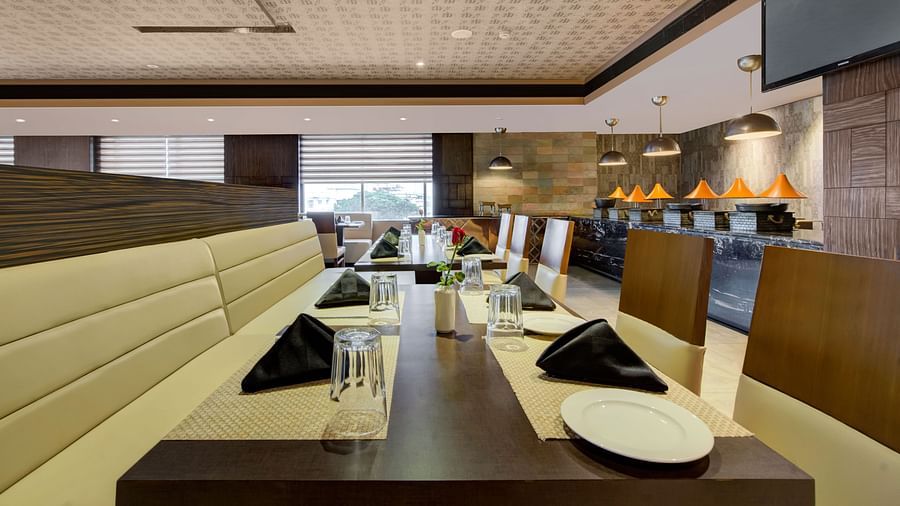 Contemporary restaurant interior with beige cushioned booths, neatly set tables, and warm ambient lighting at Voyage Milestone Hotel and Banquet Siliguri