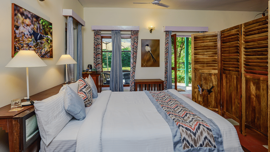 Bright heritage style bedroom with beds wooden furniture patterned textiles and ample natural light offering a restful stay at Neemrana’s Glasshouse on The Ganges suited for families or companions travelling together
