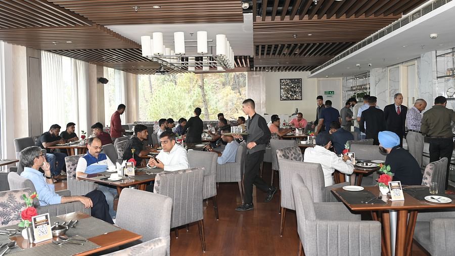 A lively and elegant restaurant setting with Refex team members and guests engaged in conversation and dining, as servers move around efficiently in a warm, well-lit atmosphere with modern wooden interiors - The Zion, Shimla.