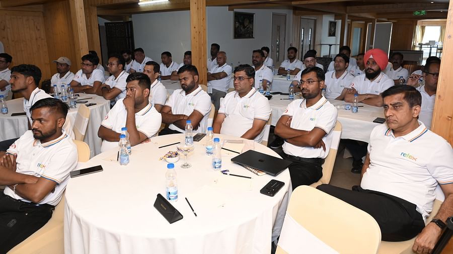 Group of professionals in white 'Refex' shirts attentively participating in a conference or training session in a wooden-panelled meeting room - The Zion, Shimla.