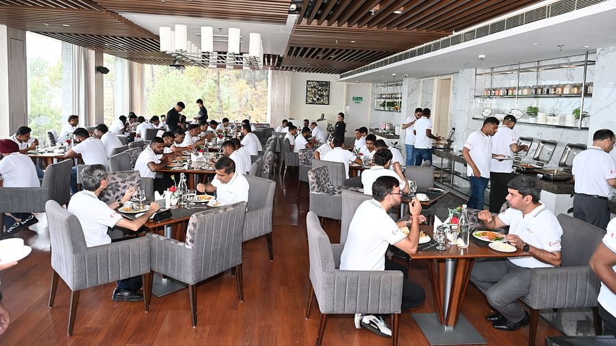 Group of people in white uniforms dining in a modern restaurant with buffet service and large windows - The Zion, Shimla.